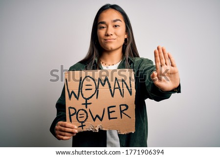 Beautiful activist asian woman asking for women rights holding banner with power message with open hand doing stop sign with serious and confident expression, defense gesture
