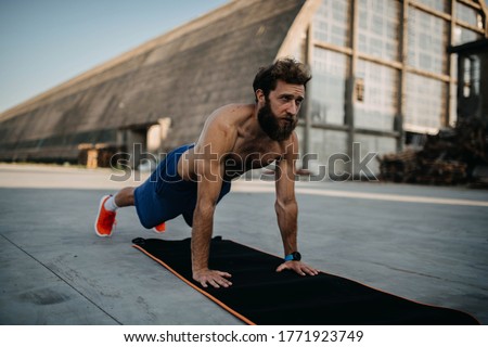 A long-bearded athlete in a plank position in front of the hangar