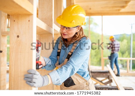 Female worker at construction site during work with wood frame house