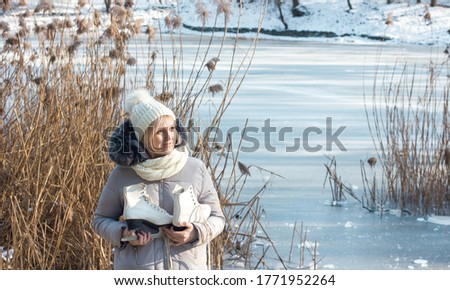  girl in winter clothes and a hat with figure skates on the background of a frozen lake, the theme of a healthy lifestyle and outdoor activities in winter, rear view, space for text