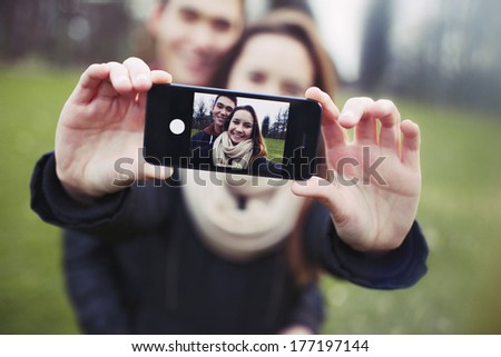 Affectionate young couple taking a self-portrait with a smartphone at the park. Mixed race teenage man and woman outdoors taking their picture with mobile phone.