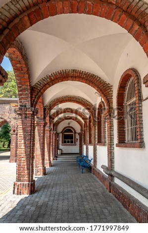 Long corridor with brick columns, arches, white walls and blue benches