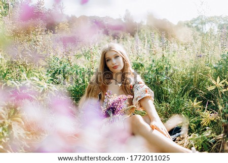 Sweet girl in the field of lupins. A girl in a beautiful dress on a field among purple flowers.