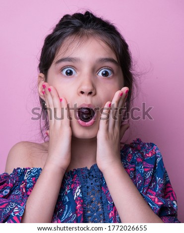Wow. Studio shot of emotional adorable little girl raising eyebrows and covering open mouth with hand being surprised and shocked, showing true astonished reaction on unexpected news. foolish grimaces