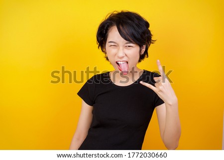 Portrait of a crazy asian girl showing tongue horns up gesture, expressing excitement of being on concert of band.