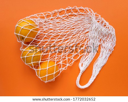 White string cotton eco bag with oranges on orange background. Monochrome simple flat lay. Ecology zero waste concept. Stock photo.