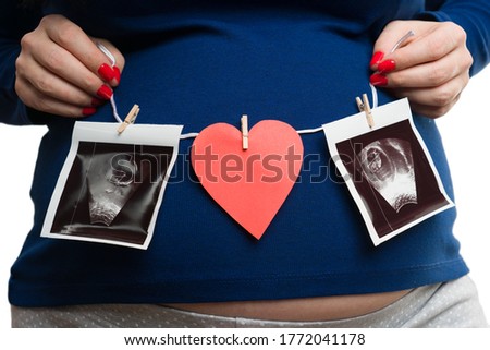 Woman showing ultrasound pictures and red heart on pregnant tummy isolated on white studio background