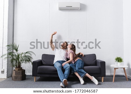 smiling girlfriend and boyfriend hugging at home with air conditioner Royalty-Free Stock Photo #1772046587
