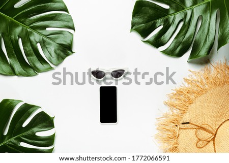 top view of green palm leaves, straw hat, sunglasses and notepad with smartphone on white background