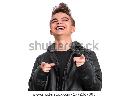 Portrait of teen boy student with spooking make-up, isolated on white background. Teenager in style of punk goth dressed in black laughing and pointing fingers to camera. Problems of transitional age