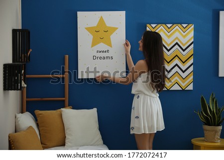 Decorator hanging picture on blue wall. Children's room interior design