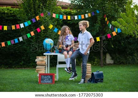 Cute blond young kids in school uniform posing at the school outdoor decoration against flags background. Copy space.