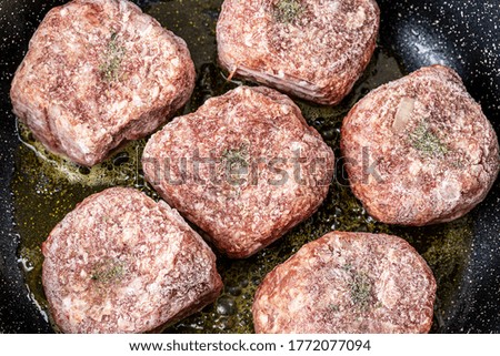 Raw beef cutlets, heated in a ceramic black skillet with vegetable oil. The process of frying steaks. Traditional cuisine.