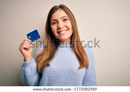 Young blonde woman holding credit card as payment over isolated background with a happy face standing and smiling with a confident smile showing teeth