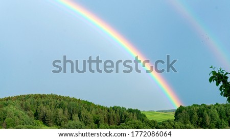 Double rainbow on a gray sky after rain. A rare atmospheric phenomenon after a storm. Beautiful hilly landscape with a real rainbow after rain on a summer day. Royalty-Free Stock Photo #1772086064