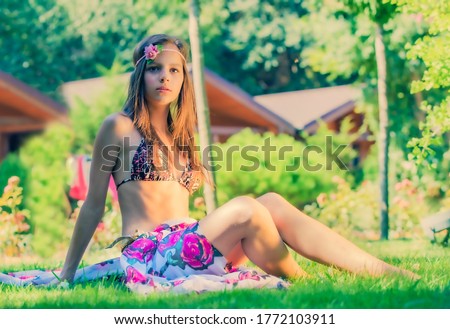 Portrait of beautiful cute brunette teenager model with makeup, poreo, in summer colorful swimsuit posing on the sea coast. young young girl in a bathing suit sitting on the grass. Copy space