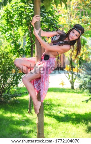 Teen girl in a swimsuit and poreo climbed a tree. portrait of a glamorous beauty in a summer park.