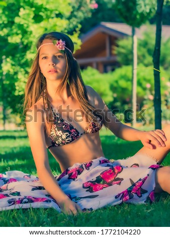 Portrait of a beautiful cute brunette teenager model with makeup, poreo, in summer swimwear posing on the seashore. young young girl in a swimsuit sits on the grass on the background of the bungalow