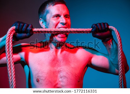 Studio image of a man in gloves bites a rope 