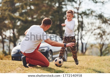 Playing soccer. Father with his son spending weekend together outdoors near forest at daytime.