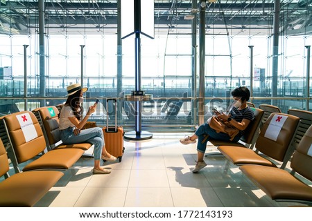 Asian female tourist wearing mask using mobile phone searching airline flight status and sit social distancing chair in airport during coronavirus or covid-19 virus outbreak a new normal concept Royalty-Free Stock Photo #1772143193