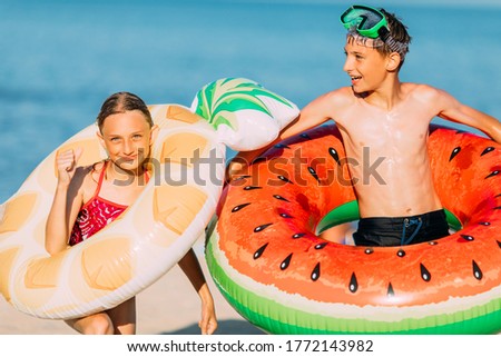 Happy kids little boy and girl have fun on the beach with inflatable swimming circles. Travel, summer holidays
