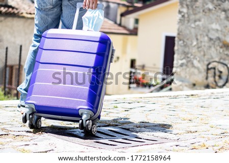 Traveller post  lockdown girl with purple suitcase and surgical mask ready to face pandemic trip