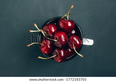 Red ripe cherries in a white iron mug in the center of a dark background. Cherries isolated on dark background. Close-up of cherries. Background with copy space