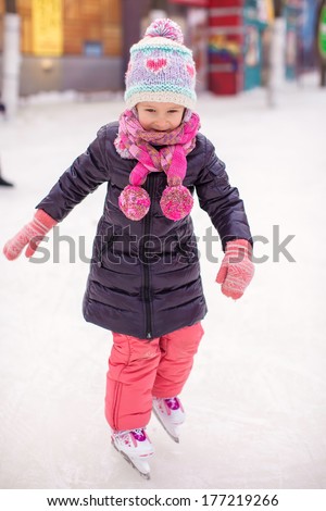Adorable happy little girl enjoying skating at the ice-rink