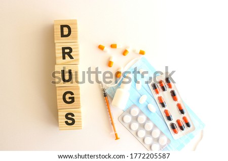 The words DRUGS is made of wooden cubes on a white background with medical drugs and medical mask. Medical concept.