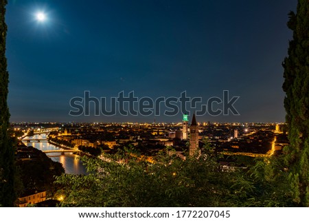 Night photo with moon in sky view along Adige river with view of Ponte Nuovo and Ponte Navi with church of Santa Anastasia and Torre di Lamberti, city of Verona, Italy.