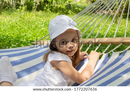 A girl in a white Panama hat is lying on a striped hammock. Summer and holidays. The girl smiles. The concept of summer vacation