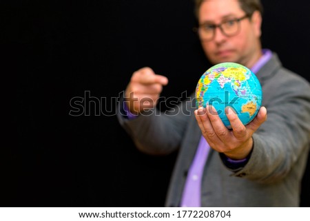 Selective focus Close up of businessman wears suit with eye glasses holding digital globe in palm shows at globe. global business communications concept.Black studio background.