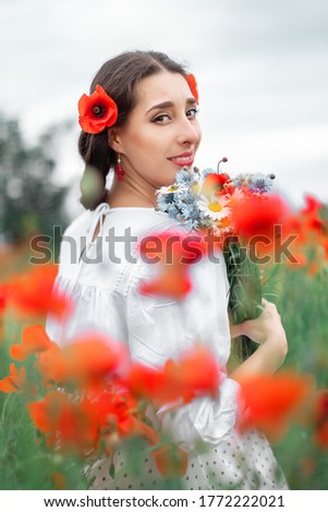 Young pretty girl Slavic or Ukrainian posing in folk dress on a flowering poppy field.