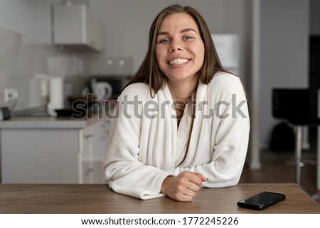 happy cheerful woman smiling looking at the video camera. Video blog at home in the kitchen. Bath white bathrobe. Make video calls.