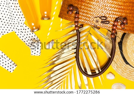 Summer background Beach accessories. Beach wicker straw rattan women's eco bag white dress hat golden tropical leaf juice in glass jars straws shells starfish on yellow background. Flat lay top view