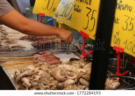A picture of fresh raw squid on sticks on ice ready to sell in a street food night market, Bangkok, Thailand 