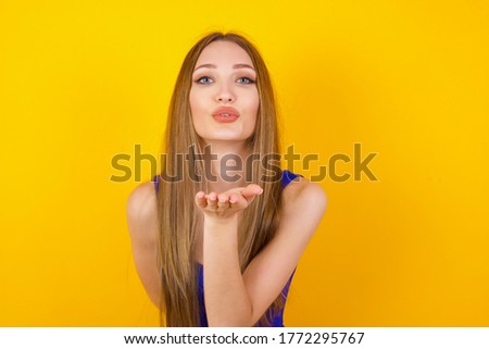 Cute appealing female blows kiss at camera, demonstrates love to boyfriend or says goodbye on distance, isolated over white studio background. Attractive young woman shows sympathy to someone.