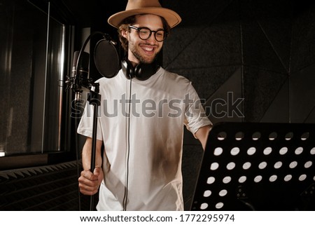 Handsome cheerful male singer happily recording new song in modern sound studio 