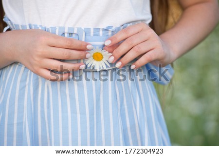 Daisy flower in the hands of a girl on the background of a dress. Light summer Manicure with Chamomile on one nail.