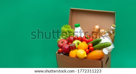 Big box with food supplies crisis food stock for quarantine isolatio.n period on green.Vegetables, oil, herbs, bread isolated.Quarantine,coronavirus,food delivery, Donation.Copy space.Top view.Banner