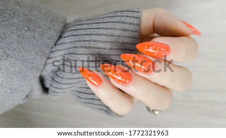 Woman hand with long nails and orange ginger manicure holds a bottle of nail polish