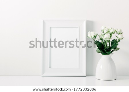 Home interior floral decor on white shelf. Front view blank mock up of photo frame. Beautiful flowers white roses in vase on white background.