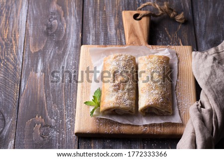 Sweet Mexican chimichanga with banana and strawberries, sprinkled with powdered sugar on a wooden table. top view. space