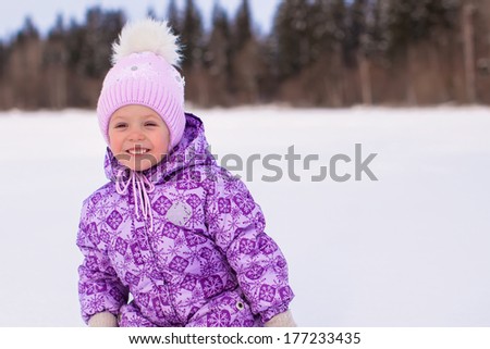 Little happy adorable girl having fun on the snow at winter sunny day