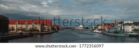 Horizontal image of buildings near canal and boats in harbor with cloudy sky at background in Copenhagen, Denmark