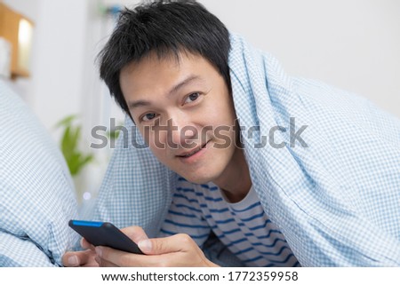 Asian man guy chatting with friends on smartphone, lying on bed at home, copy space.
