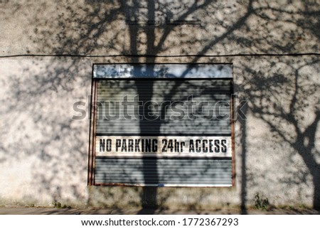 No Parking Sign on Industrial Metal Shutter with Shadows of Trees on Wall 