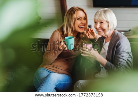 Happy senior mother with adult daughter sitting on couch and holding cups with coffee or tea at home. Togetherness concept Royalty-Free Stock Photo #1772373158