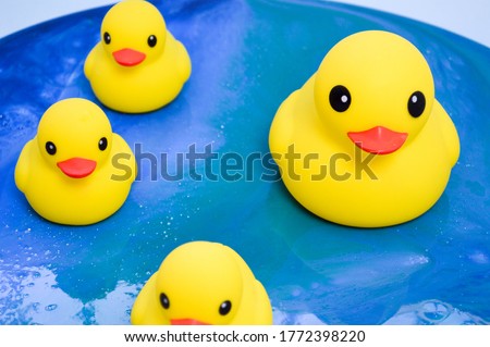 yellow rubber ducks floating on the ocean surface of epoxy. decorative toys stand on a glossy interior picture in the form of water with sun glare. abstract background.